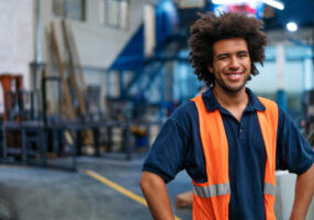 Portrait of a happy young man working in warehouse. Male warehouse worker in uniform looking at camera and smiling.